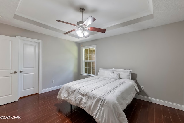 bedroom with dark hardwood / wood-style flooring, ceiling fan, and a raised ceiling