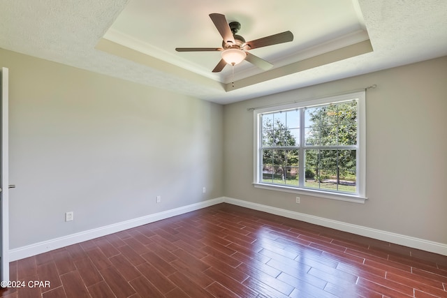 empty room featuring dark wood-type flooring, ceiling fan, a tray ceiling, and a textured ceiling