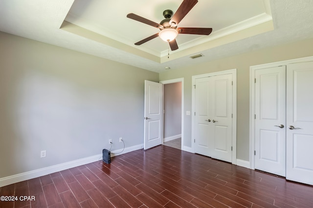 unfurnished bedroom featuring a tray ceiling, ceiling fan, and dark hardwood / wood-style flooring