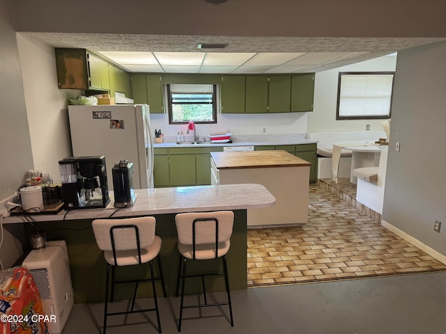 kitchen with wood counters, sink, a breakfast bar area, green cabinetry, and white fridge