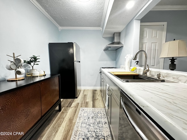 kitchen with crown molding, light wood-type flooring, a textured ceiling, wall chimney range hood, and appliances with stainless steel finishes