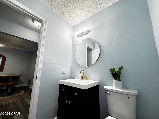 half bath with baseboards, toilet, wood finished floors, a textured ceiling, and vanity