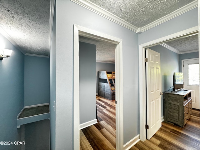 corridor with a textured ceiling, ornamental molding, dark wood finished floors, and baseboards