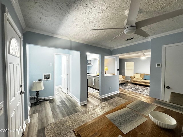 interior space featuring ceiling fan, a textured ceiling, wood finished floors, visible vents, and ornamental molding