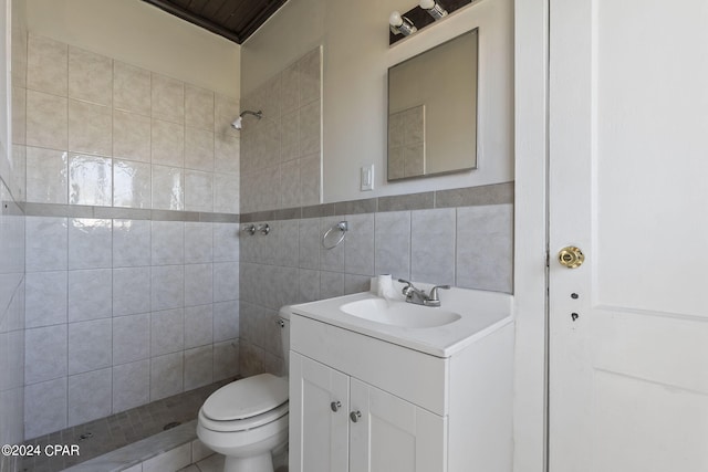 bathroom with vanity, toilet, a tile shower, and tile walls