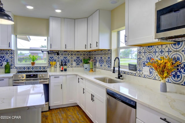 kitchen with light stone countertops, pendant lighting, white cabinets, appliances with stainless steel finishes, and sink