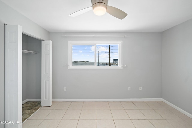 unfurnished bedroom with a closet, baseboards, a ceiling fan, and light tile patterned flooring