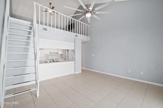 unfurnished living room featuring ceiling fan, a towering ceiling, baseboards, visible vents, and tile patterned floors