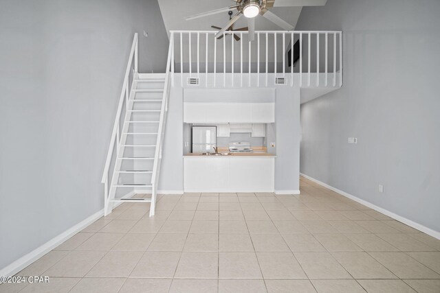 unfurnished living room with ceiling fan, a towering ceiling, and light tile patterned floors