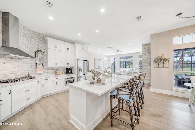 kitchen with gas cooktop, visible vents, high end fridge, wall chimney range hood, and tasteful backsplash