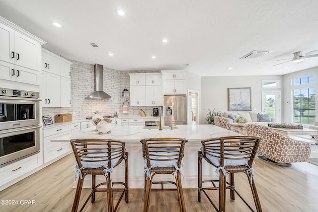 kitchen featuring stainless steel appliances, visible vents, light wood-style flooring, and wall chimney exhaust hood