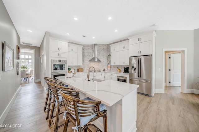 kitchen with visible vents, a sink, stainless steel appliances, wall chimney range hood, and backsplash