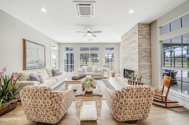 living room featuring visible vents, ceiling fan, wood finished floors, a textured ceiling, and a stone fireplace