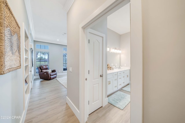 hall featuring baseboards, crown molding, and light wood-style floors