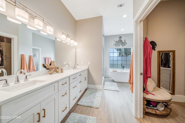 full bathroom with a freestanding tub, visible vents, a sink, and wood finished floors