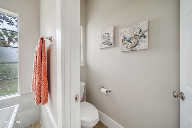 bathroom featuring toilet, baseboards, and a wealth of natural light