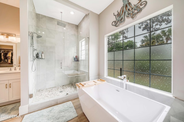 bathroom with a walk in closet, a soaking tub, a stall shower, vanity, and wood finished floors