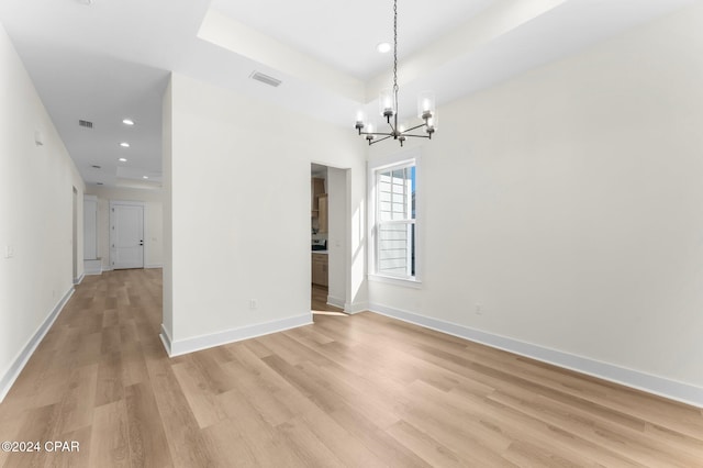 spare room featuring light wood-type flooring and a chandelier