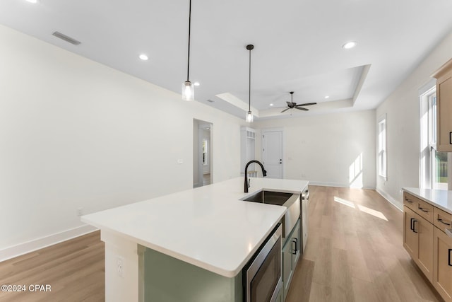 kitchen featuring a center island with sink, ceiling fan, a tray ceiling, and light hardwood / wood-style flooring