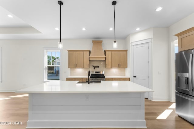 kitchen with sink, stainless steel appliances, pendant lighting, a kitchen island with sink, and custom range hood