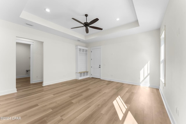 unfurnished room featuring a raised ceiling, ceiling fan, and light wood-type flooring