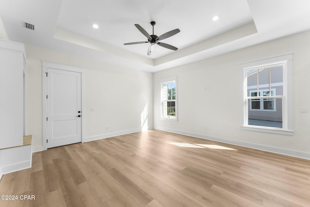 empty room featuring a tray ceiling, ceiling fan, and light wood-type flooring