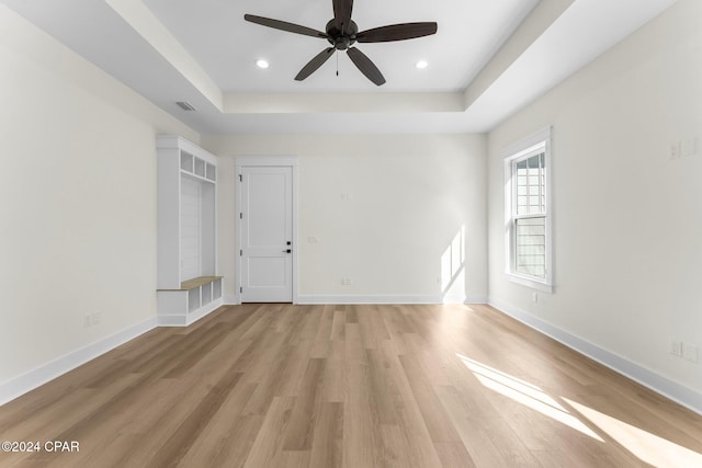 unfurnished room with light wood-type flooring, a raised ceiling, and ceiling fan