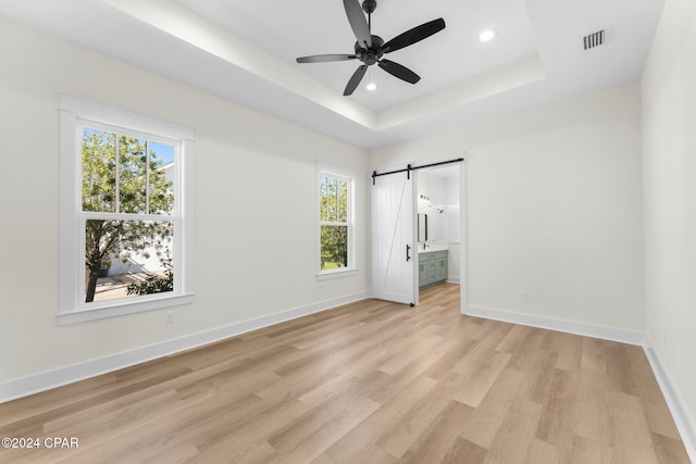 unfurnished bedroom featuring a barn door, light wood-type flooring, connected bathroom, and multiple windows