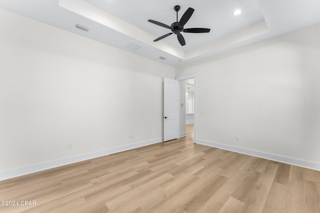 empty room featuring a tray ceiling, ceiling fan, and light wood-type flooring