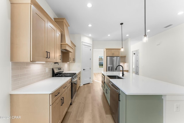 kitchen featuring a kitchen island with sink, sink, appliances with stainless steel finishes, decorative light fixtures, and light hardwood / wood-style floors