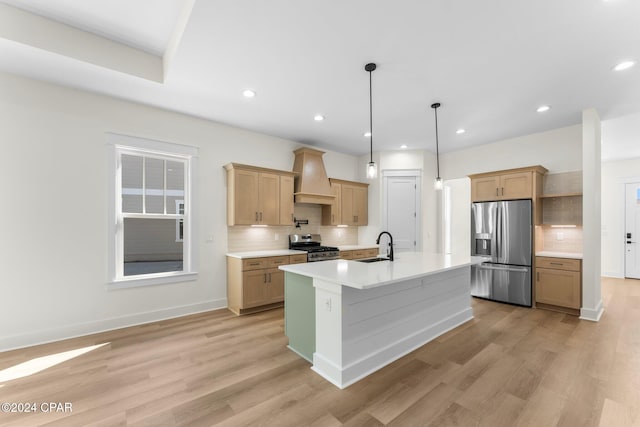 kitchen with custom range hood, a kitchen island with sink, appliances with stainless steel finishes, and light hardwood / wood-style flooring