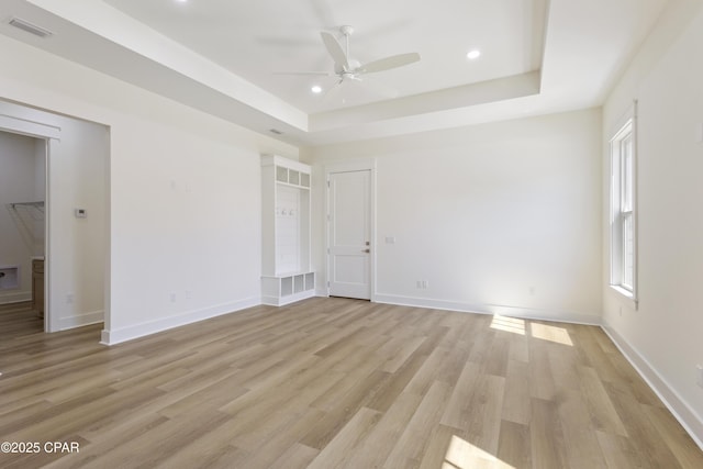 unfurnished bedroom featuring light wood-type flooring, a tray ceiling, visible vents, and baseboards