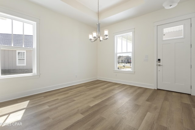 foyer entrance featuring light wood-type flooring, an inviting chandelier, baseboards, and a raised ceiling