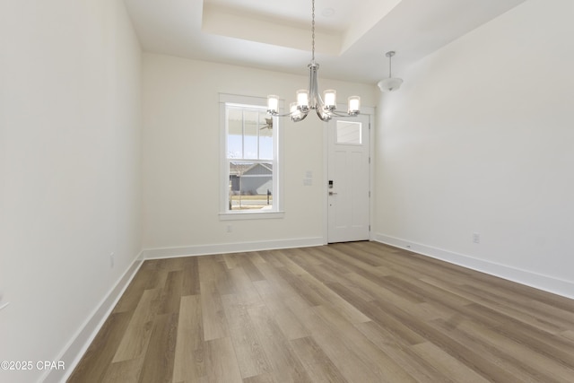 interior space with a chandelier, a tray ceiling, baseboards, and light wood finished floors