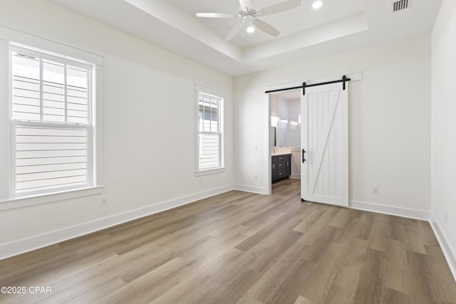 unfurnished bedroom with a barn door, visible vents, baseboards, light wood-type flooring, and a raised ceiling