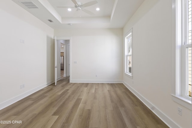 spare room featuring baseboards, visible vents, a raised ceiling, light wood-style flooring, and recessed lighting