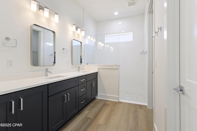 bathroom with double vanity, visible vents, a sink, wood finished floors, and walk in shower