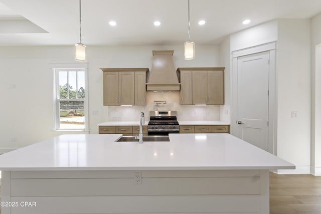 kitchen with light countertops, custom range hood, backsplash, a sink, and stainless steel gas range