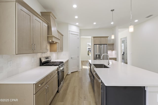 kitchen with light wood finished floors, decorative backsplash, stainless steel appliances, light countertops, and a sink