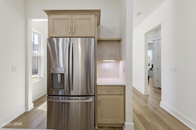 kitchen with stainless steel fridge, light brown cabinets, tasteful backsplash, and light wood-style flooring