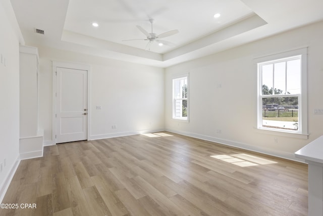 unfurnished room featuring a tray ceiling, light wood-style flooring, and visible vents