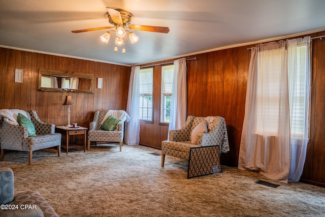 sitting room with wood walls, crown molding, carpet floors, and ceiling fan