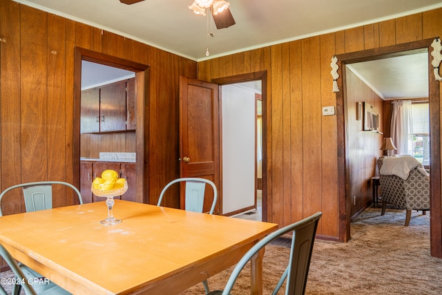 carpeted dining area featuring wood walls, ceiling fan, and crown molding