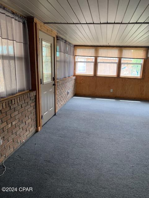 carpeted empty room featuring brick wall and wood walls