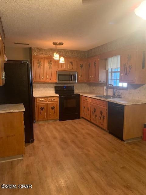 kitchen featuring a textured ceiling, black appliances, hanging light fixtures, sink, and light wood-type flooring