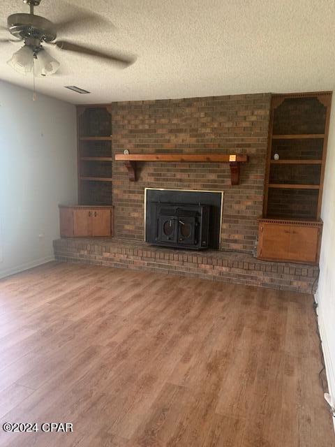 unfurnished living room with ceiling fan, hardwood / wood-style flooring, a textured ceiling, and a brick fireplace