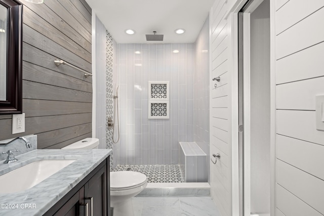 bathroom with wooden walls, tile patterned flooring, tiled shower, toilet, and vanity