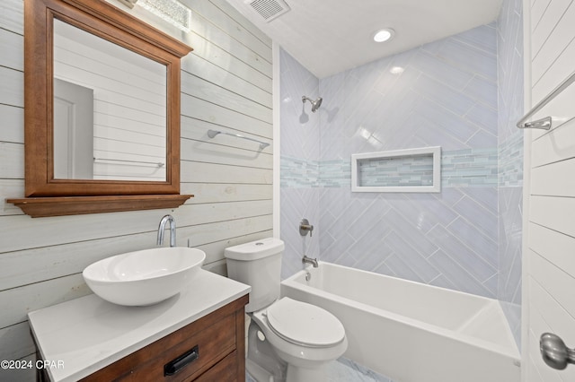 full bathroom featuring wood walls, vanity, tiled shower / bath, and toilet