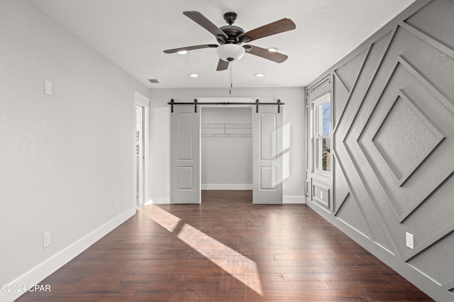 unfurnished bedroom with a closet, dark hardwood / wood-style flooring, a barn door, and ceiling fan