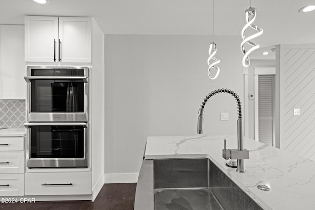 kitchen featuring white cabinetry, pendant lighting, stainless steel double oven, light stone counters, and dark hardwood / wood-style floors